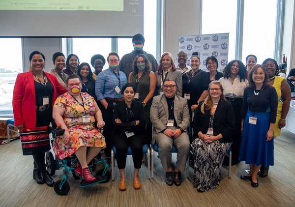 Twenty people of varying genders, ages, races, ethnicities, disabilities, and other identities pose together.